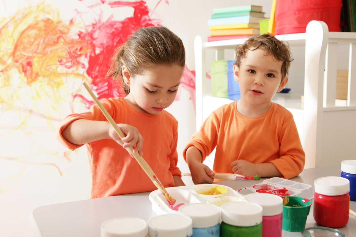 Bambini che partecipano a laboratorio creativo all'aperto a La Maddalena, tavolini colorati, sorrisi, genitori rilassati, contesto isola mediterranea
