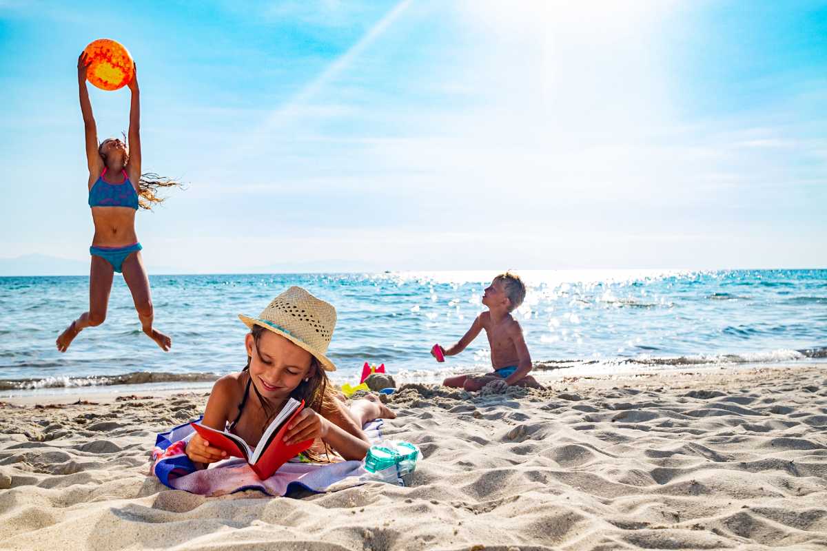 Famiglia con bambini che gioca sulla spiaggia di sabbia bianca, mare cristallino e sfondo isole La Maddalena, atmosfera rilassata e felice