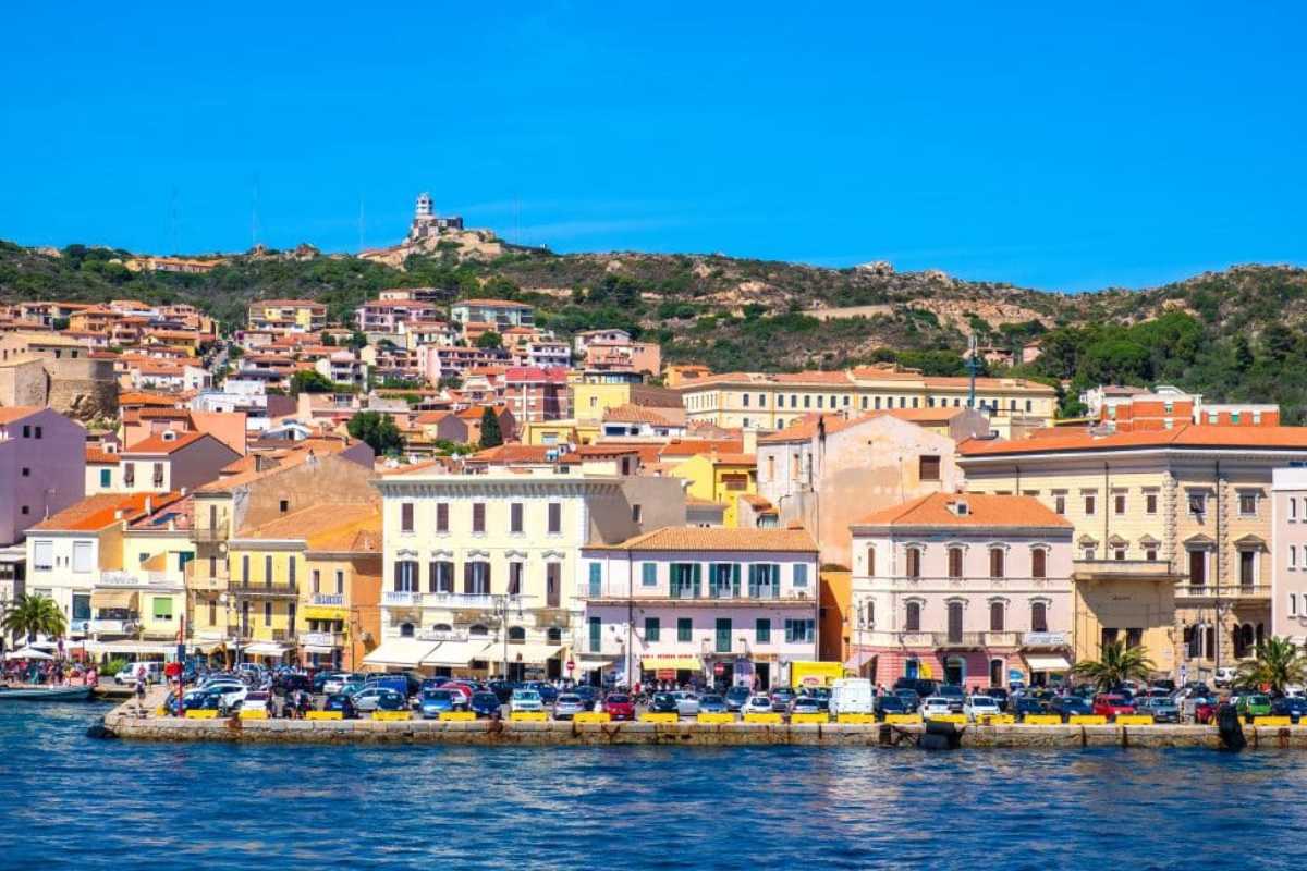 Scorcio panoramico del centro storico di La Maddalena all’ora dorata, con facciate colorate e barche ormeggiate sul lungomare, atmosfera vivace di fine giornata